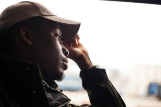 Un jeune homme pensif regarde au loin à travers une fenêtre, capturant un moment d’introspection. Crédit photo : Andriyko Podilnyk / Unsplash