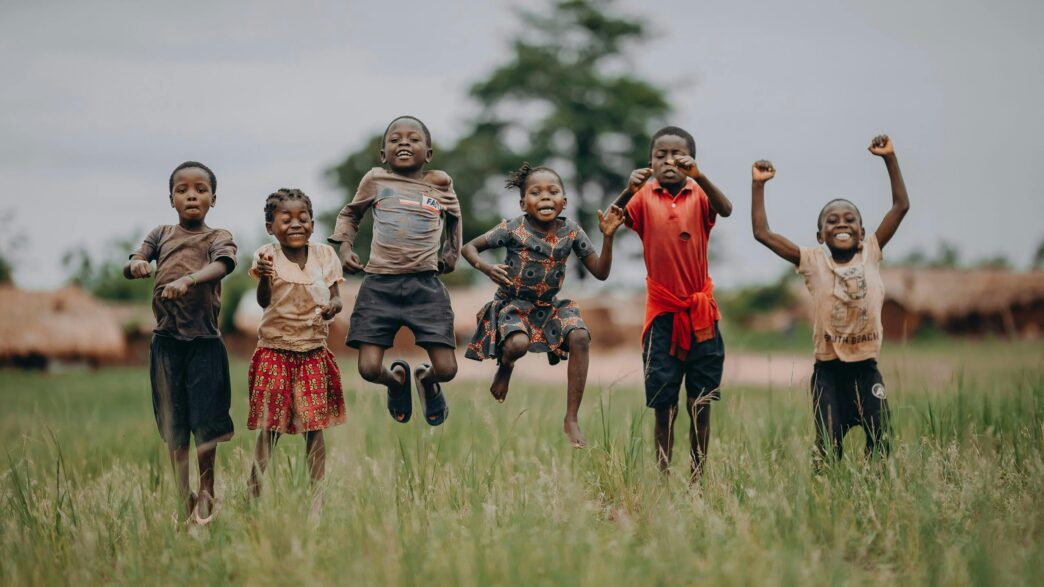 Des enfants sautent et rient dans un champ, incarnant la joie, l’espoir et la liberté que chaque enfant mérite en cette Journée dédiée à l’enfance.