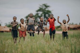 Des enfants sautent et rient dans un champ, incarnant la joie, l’espoir et la liberté que chaque enfant mérite en cette Journée dédiée à l’enfance.