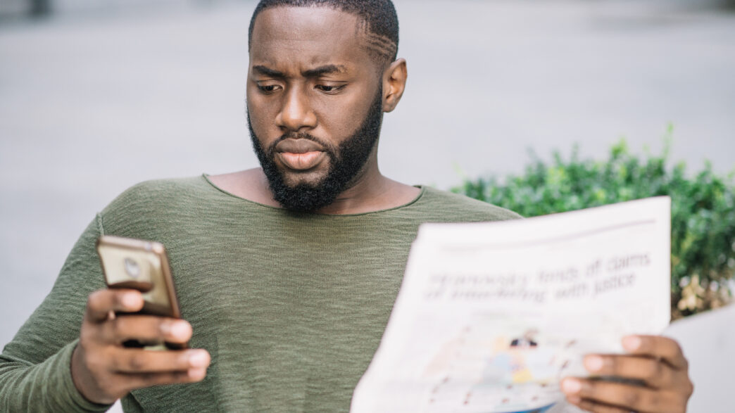 Homme sérieux avec journal en utilisant un smartphone